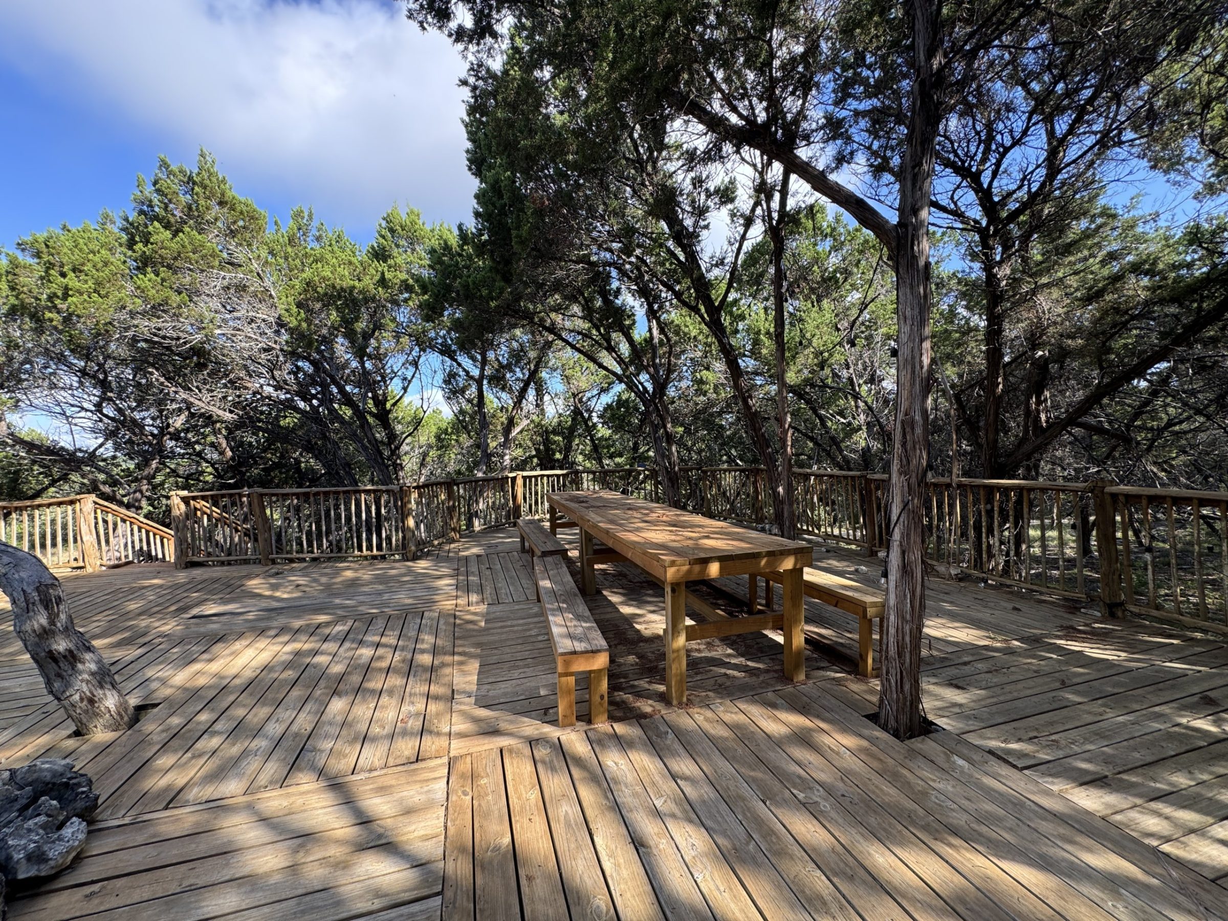 The open-air gathering deck with its long communal table under the junipers