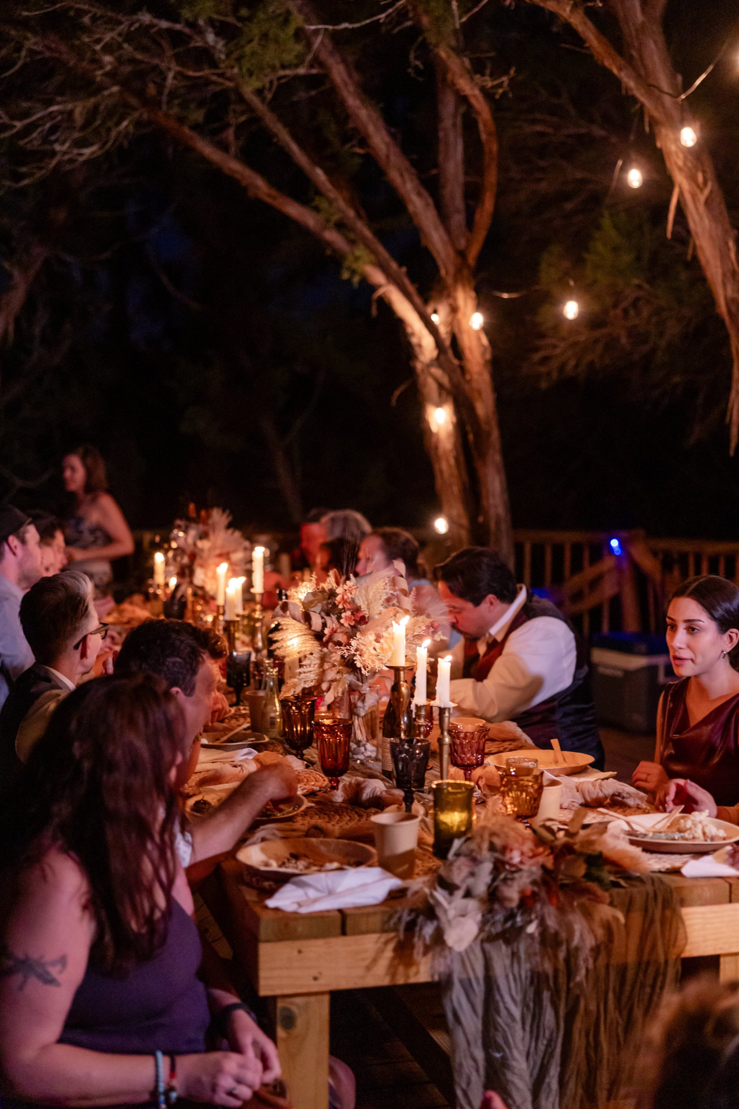 The candlelit wedding dinner at a long table under the junipers