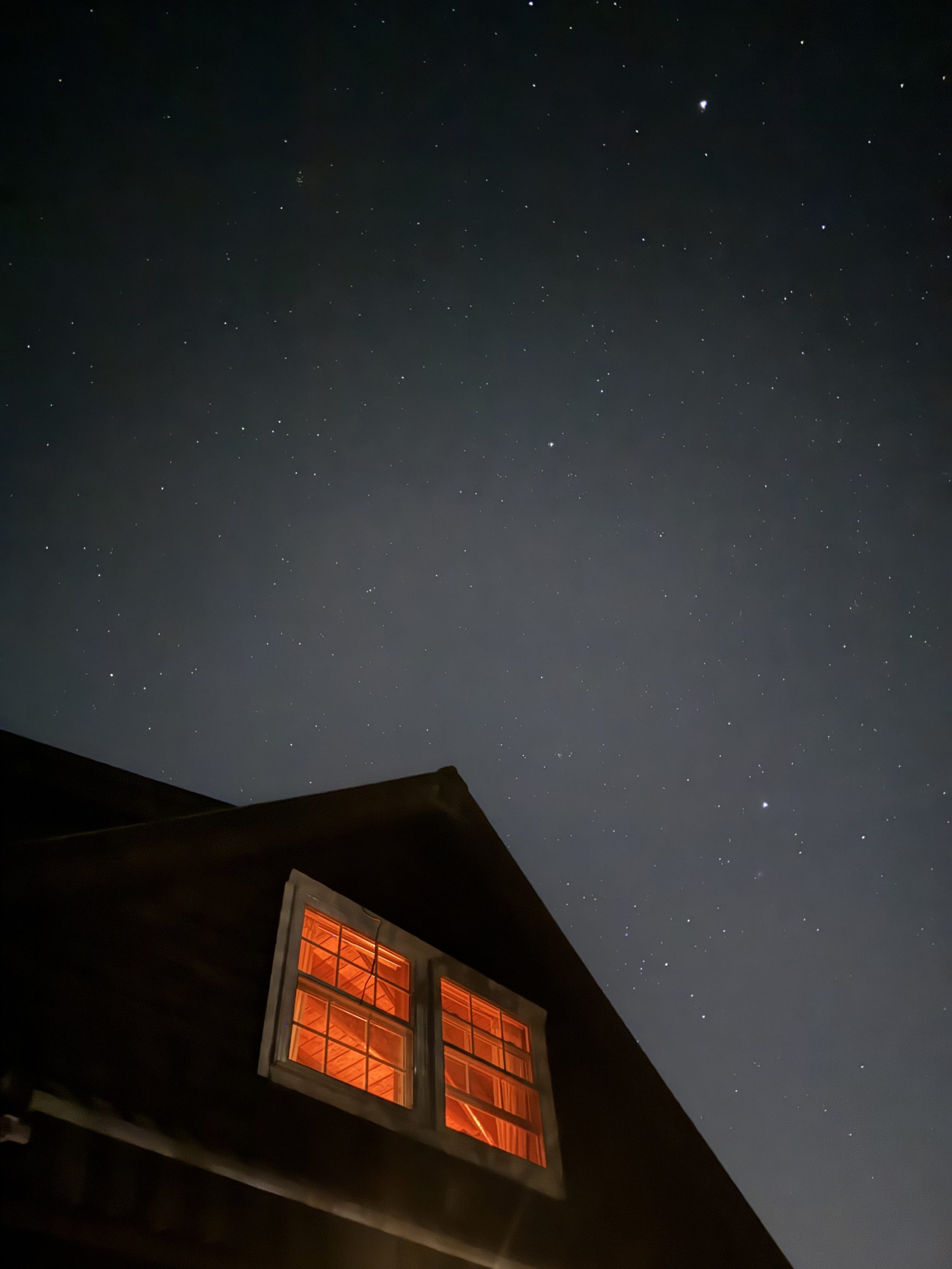 A star-filled night sky over the barn roofline, its windows glowing warm