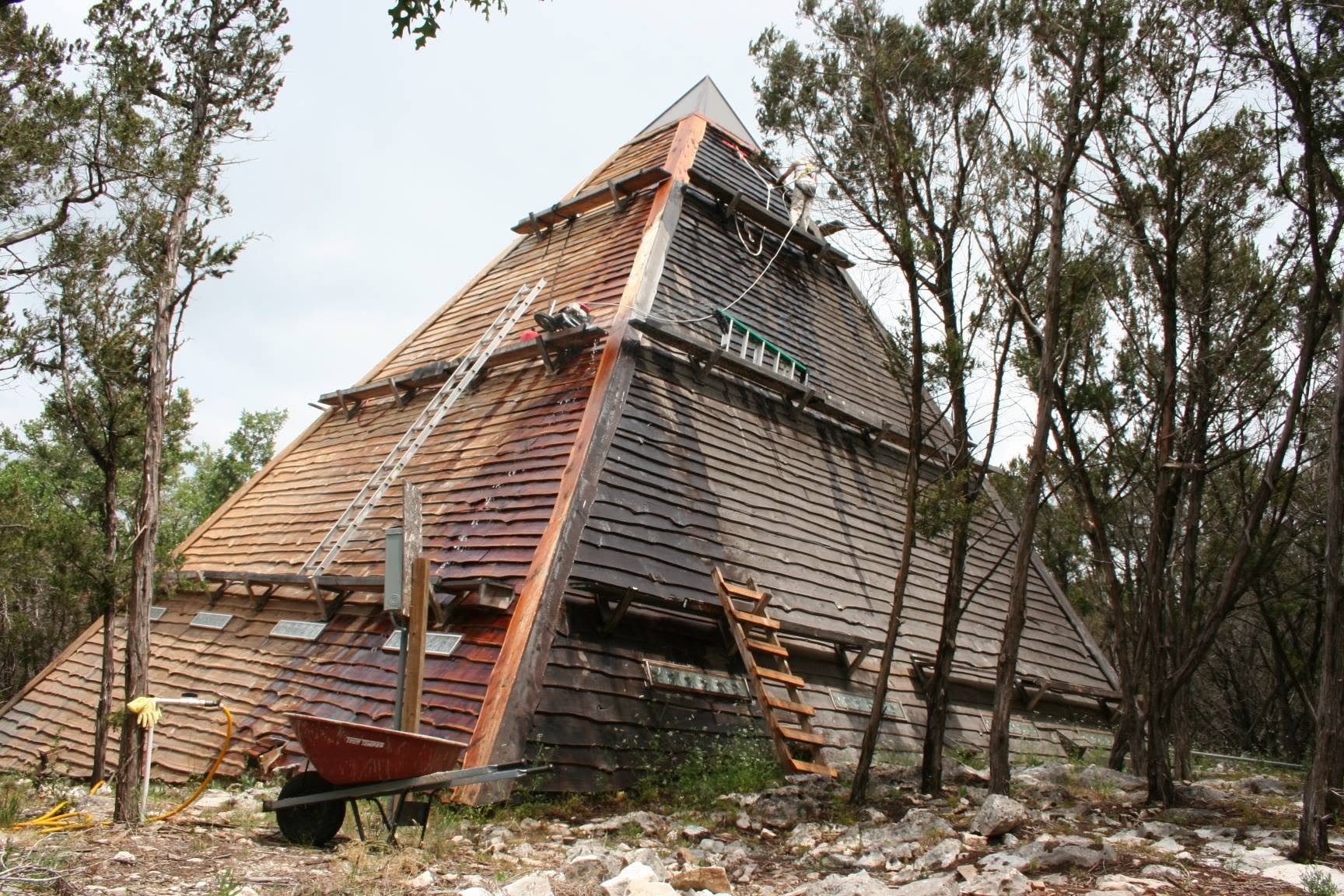 The pyramid mid-build: fresh cedar shakes going on course by course, ladders and a wheelbarrow at the base